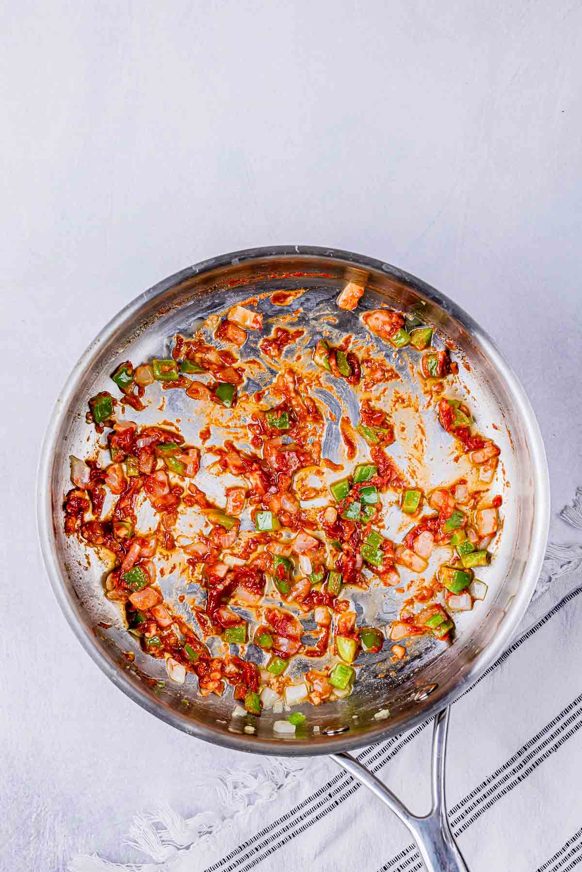 onions, peppers and tomato cooking in a skillet.