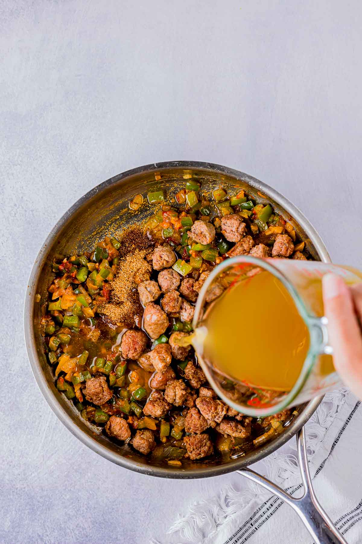 broth being poured into a skillet with sausage.