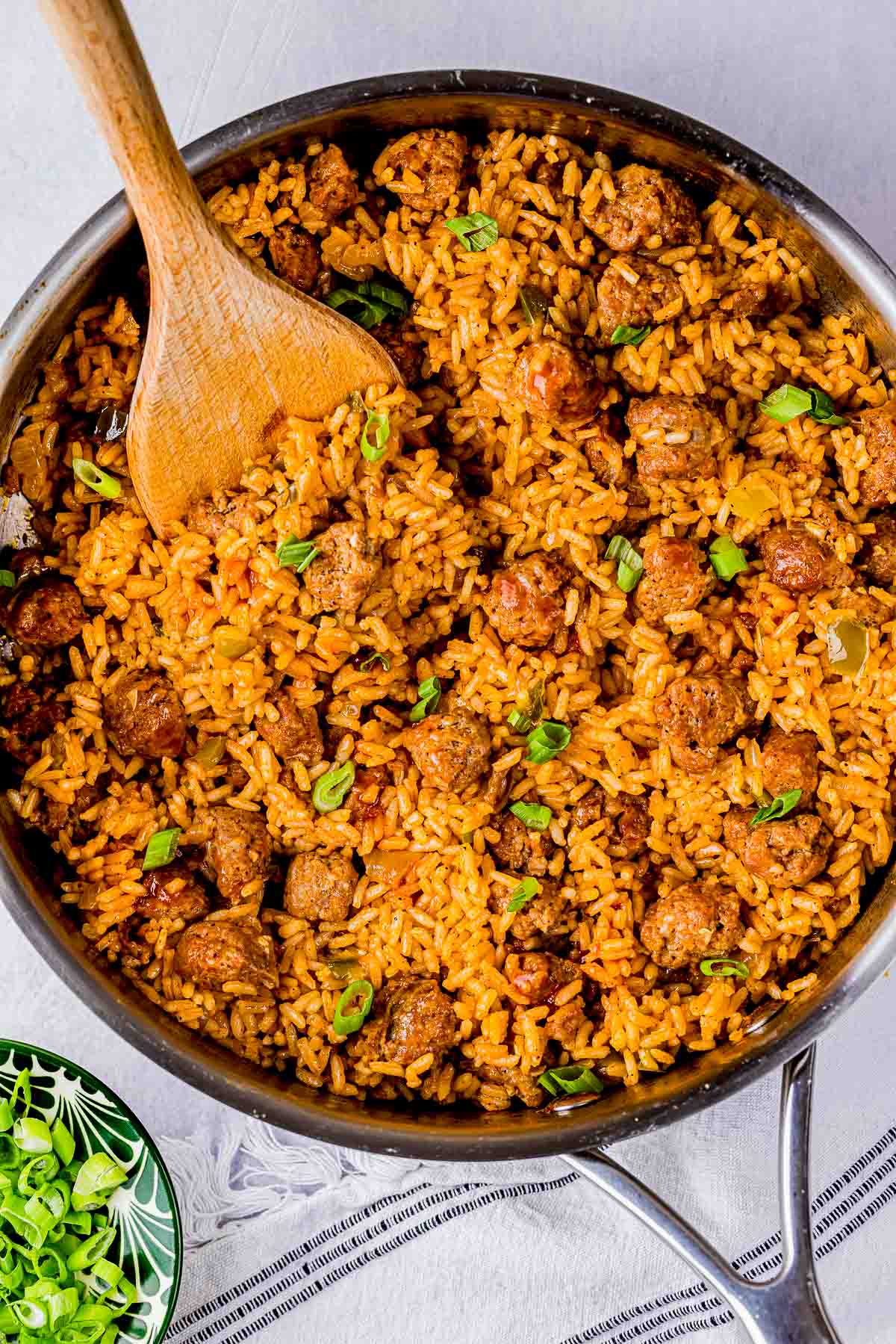 a skillet of sausage and rice garnished with green onions.