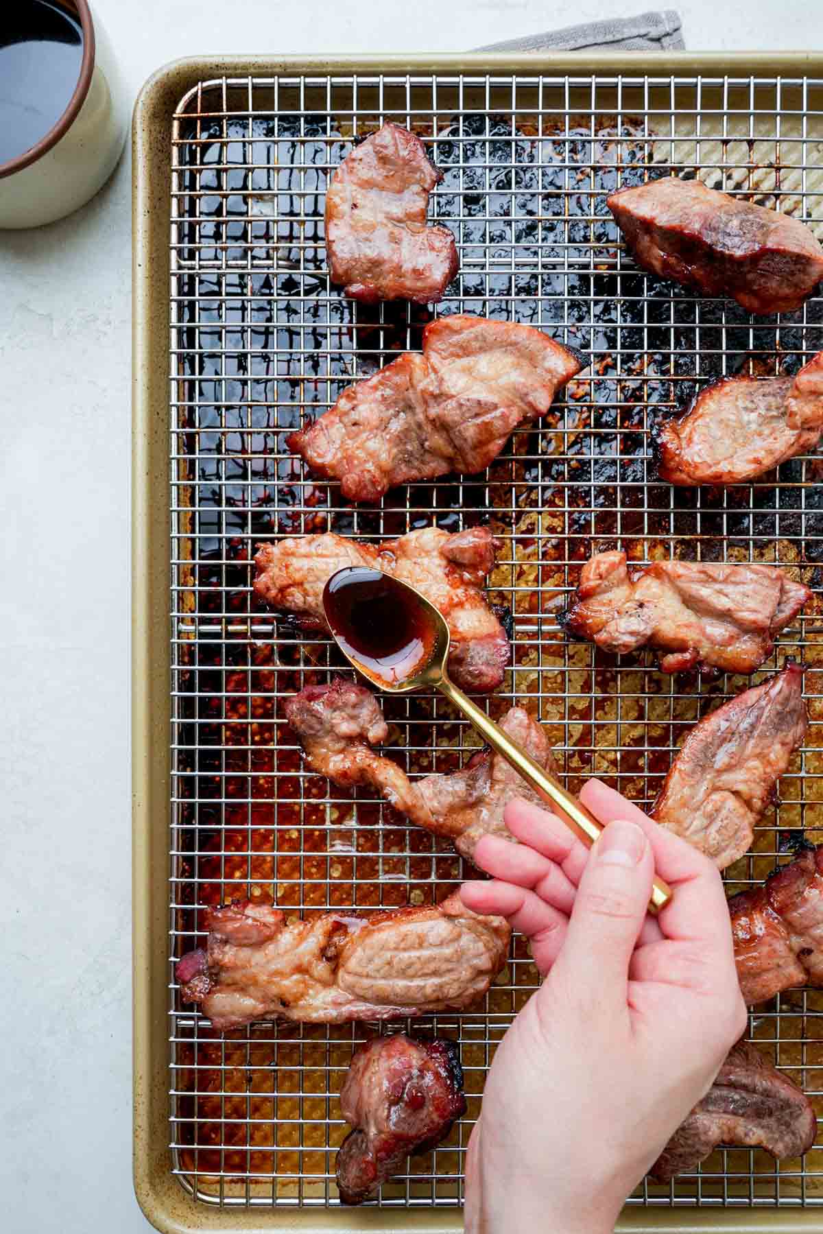 spooning sauce over roasted pork on a baking rack.