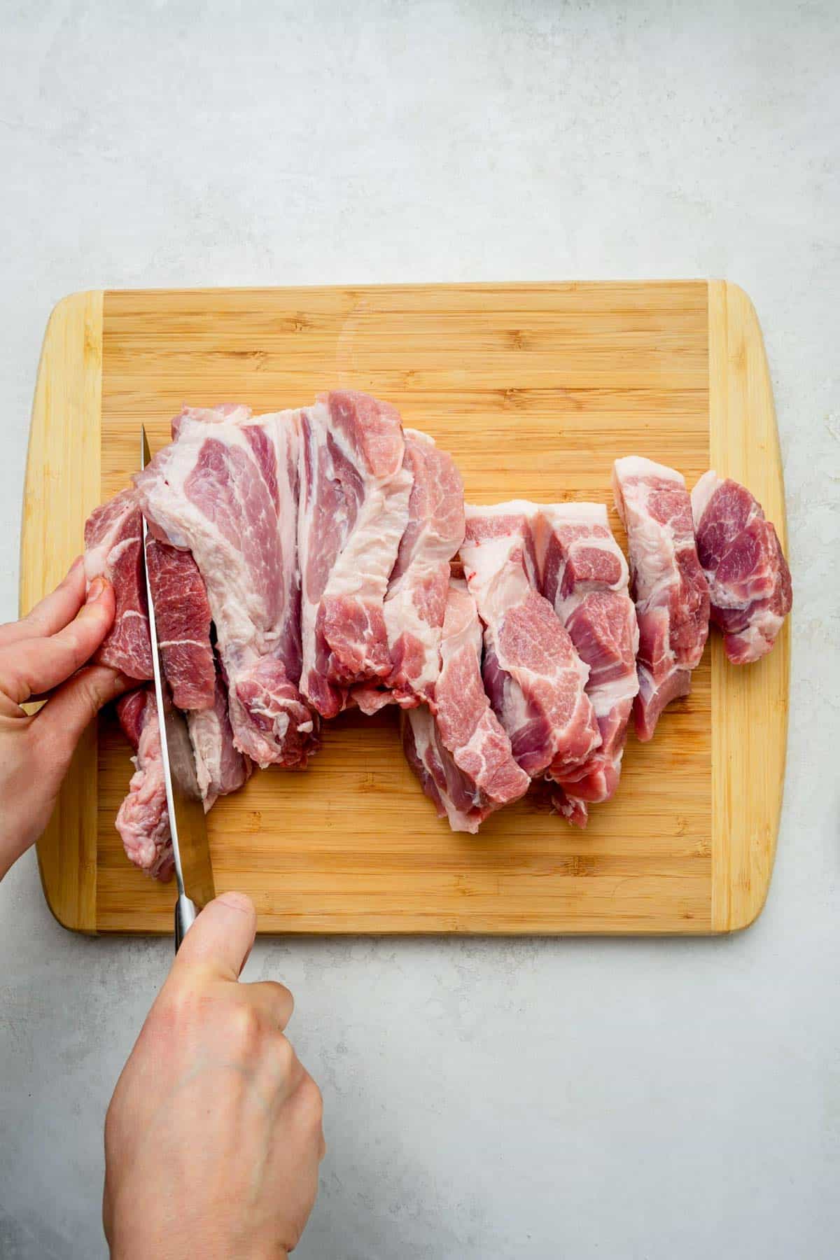 raw pork being cut into strips on a cutting board.