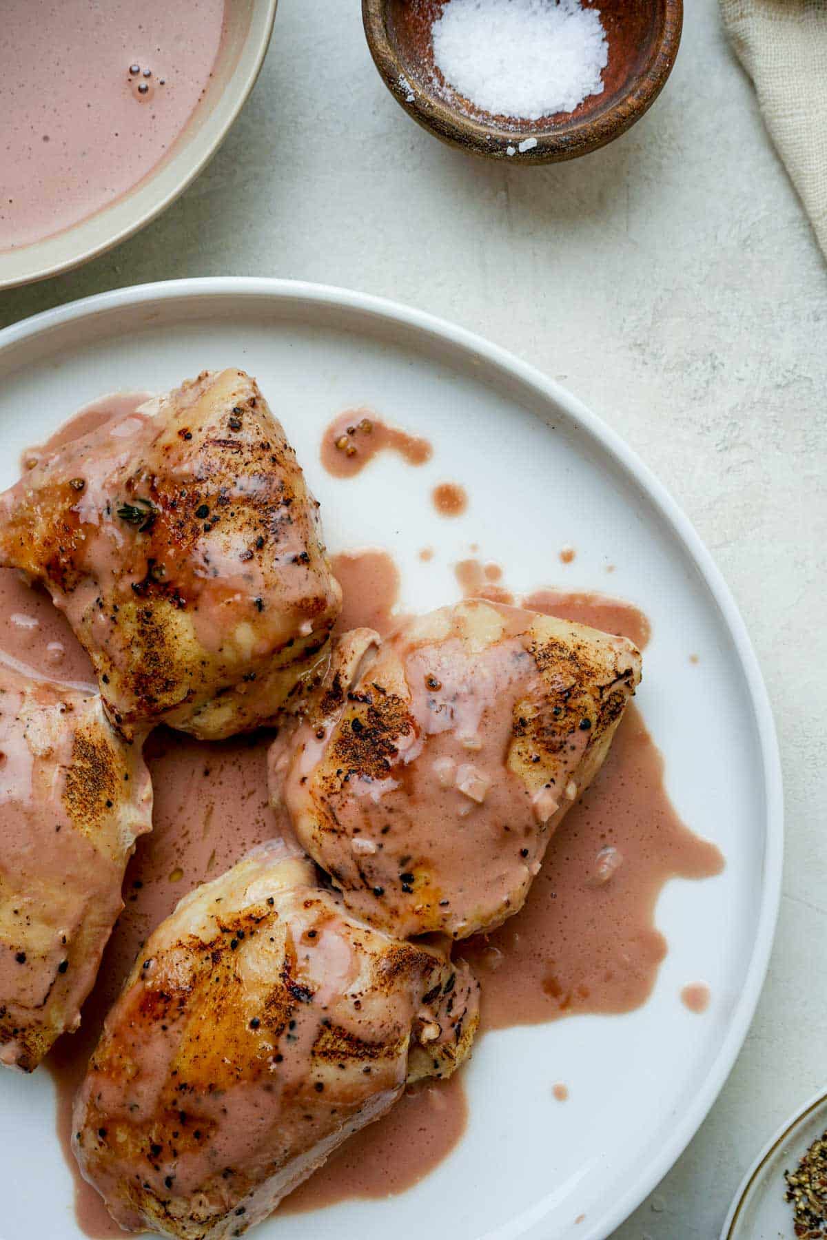 chicken thighs on a plate with pink sauce on top.