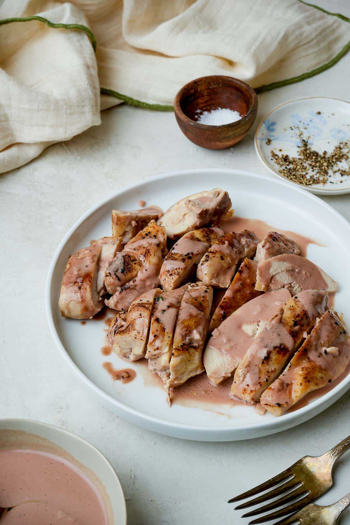 chicken thighs covered in a pink sauce and sliced on a plate.