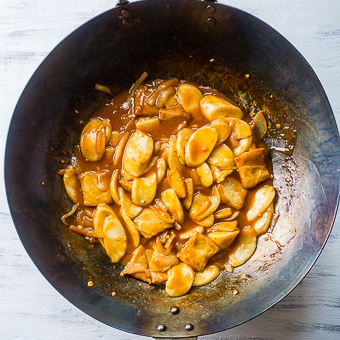 rice cakes cooking in an orange sauce in a wok.