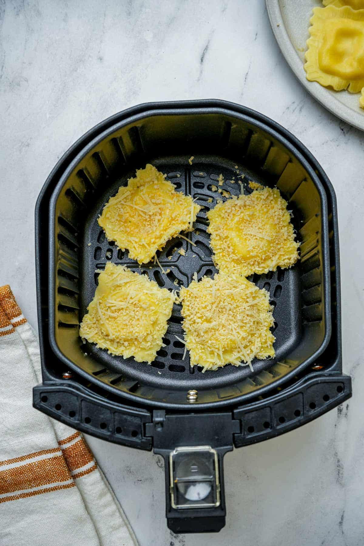 ravioli with coating in an air fryer basket.