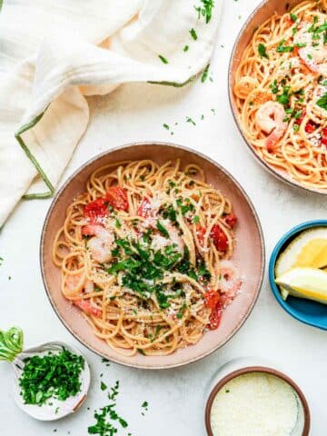 2 bowls of pasta with shrimp and parsley on top.