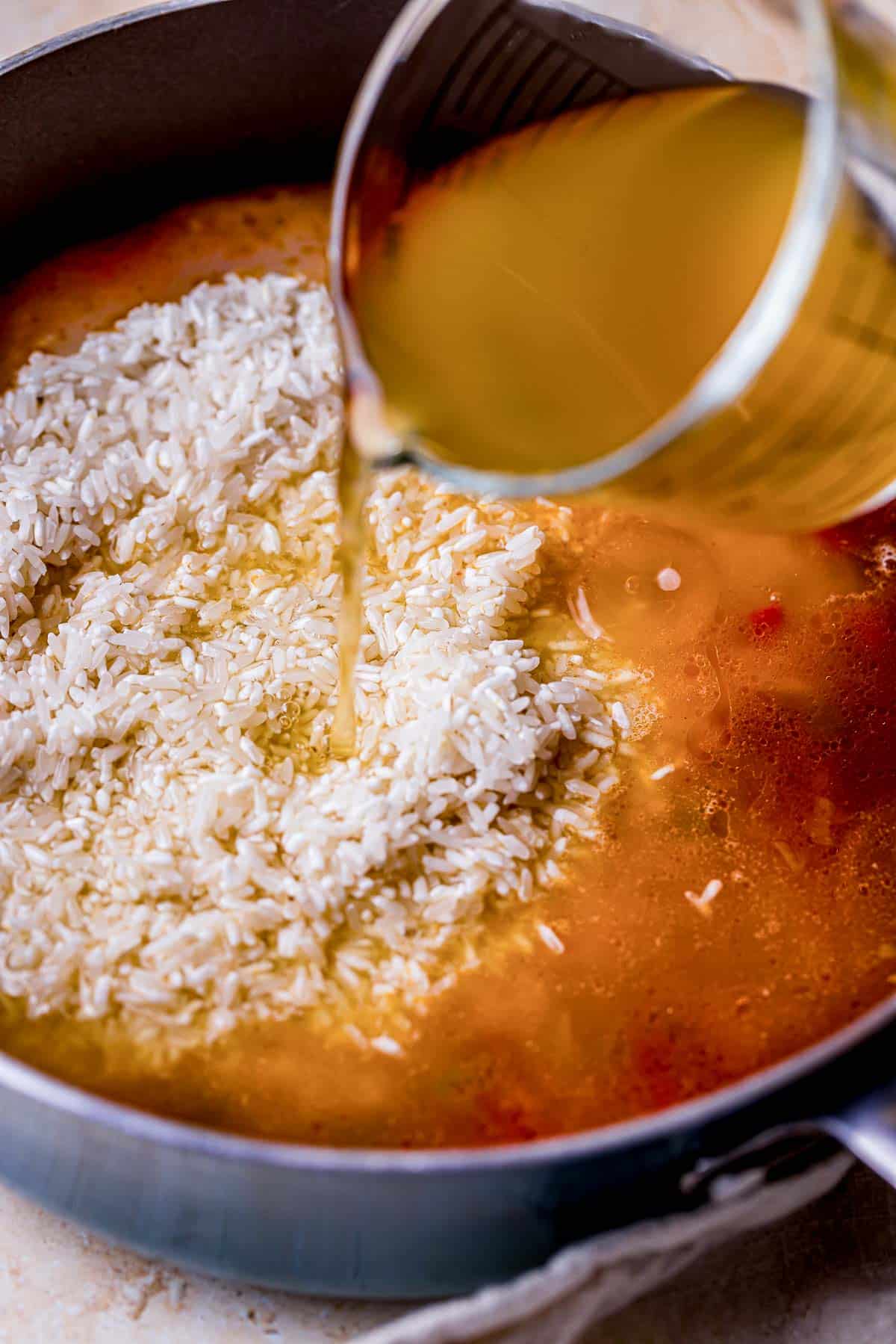 broth being poured into rice in a skillet.