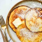 3 pancakes on a plate with powdered sugar and butter.