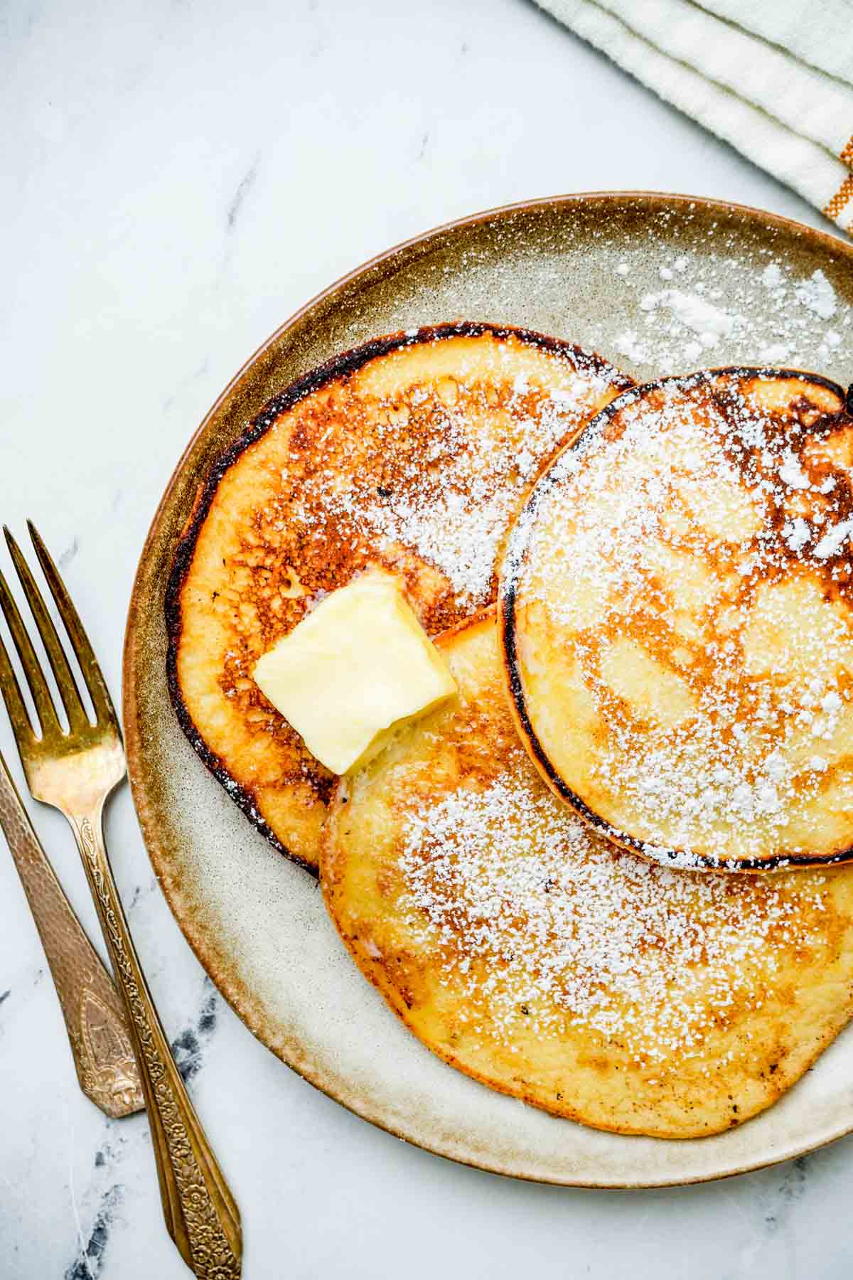 3 pancakes on a plate with powdered sugar and butter.