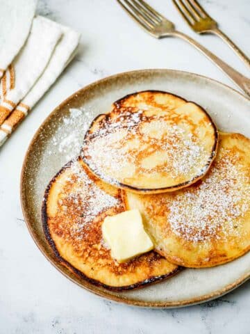 lemon pancakes with powdered sugar and butter on a white plate.