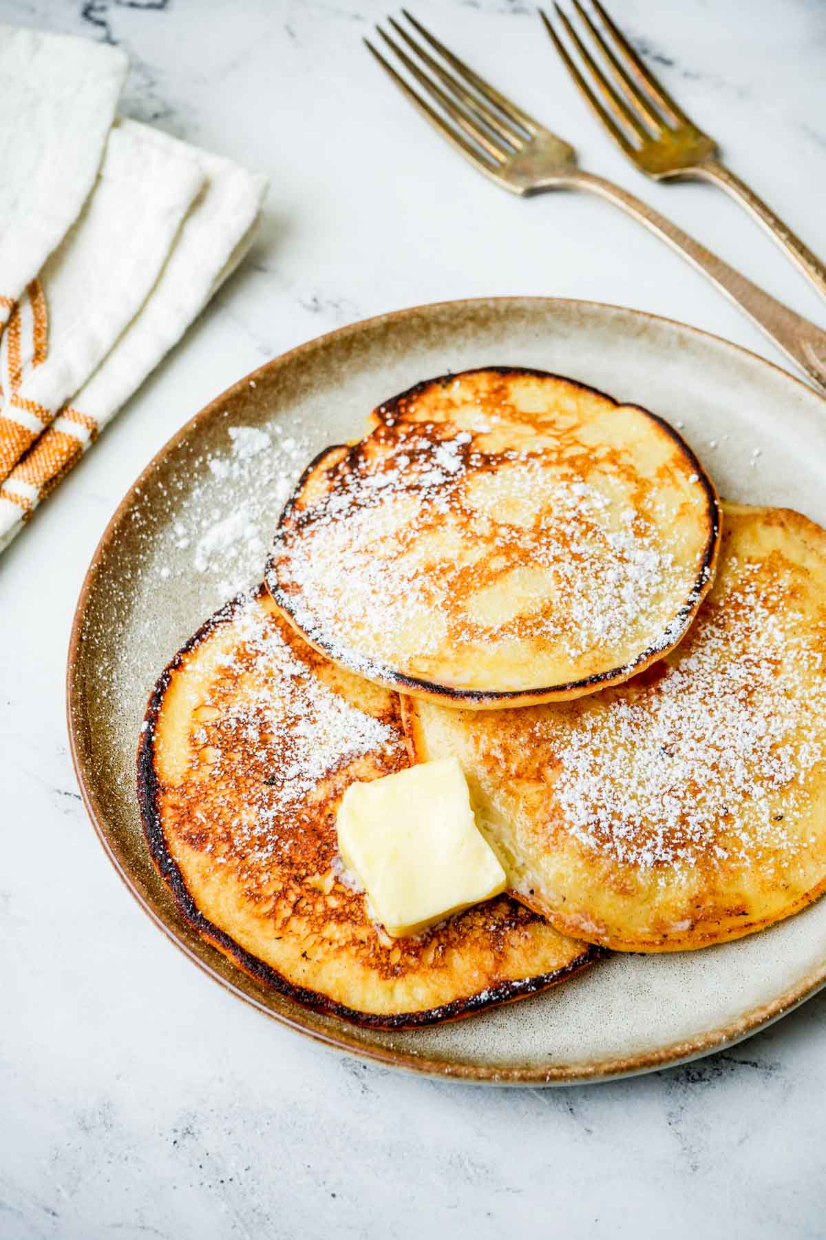 lemon pancakes with powdered sugar and butter on a white plate.