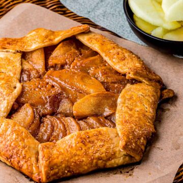 caramel apple galette on parchment paper with sliced apples in the background.