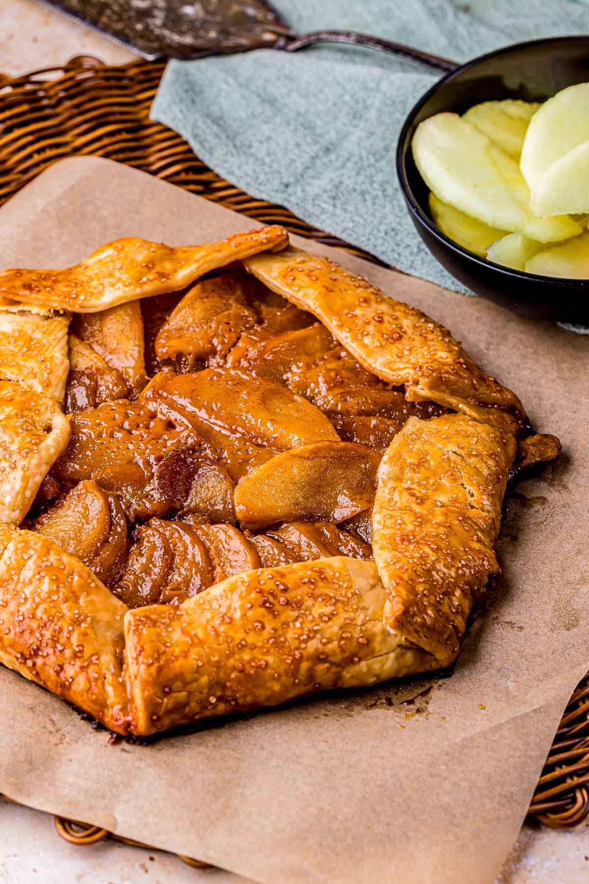 caramel apple galette on parchment paper with sliced apples in the background.