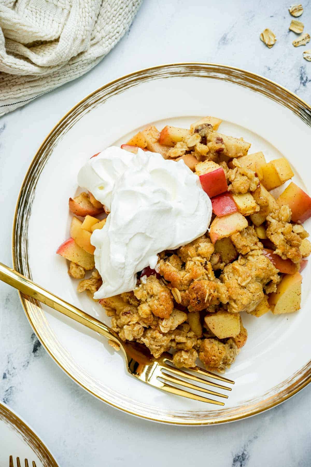 a plate of apple crisp with whipped cream and a spoon.