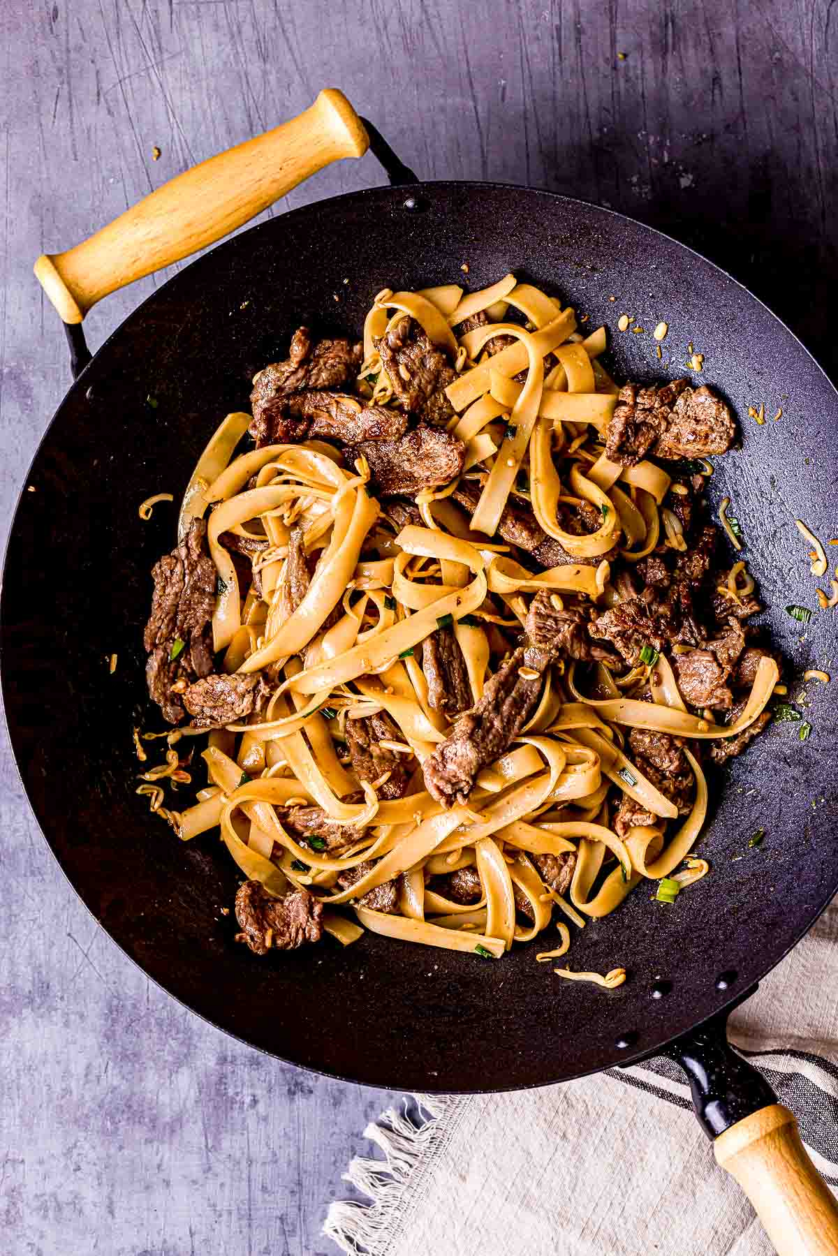 rice noodles in brown sauce with beef in a wok.