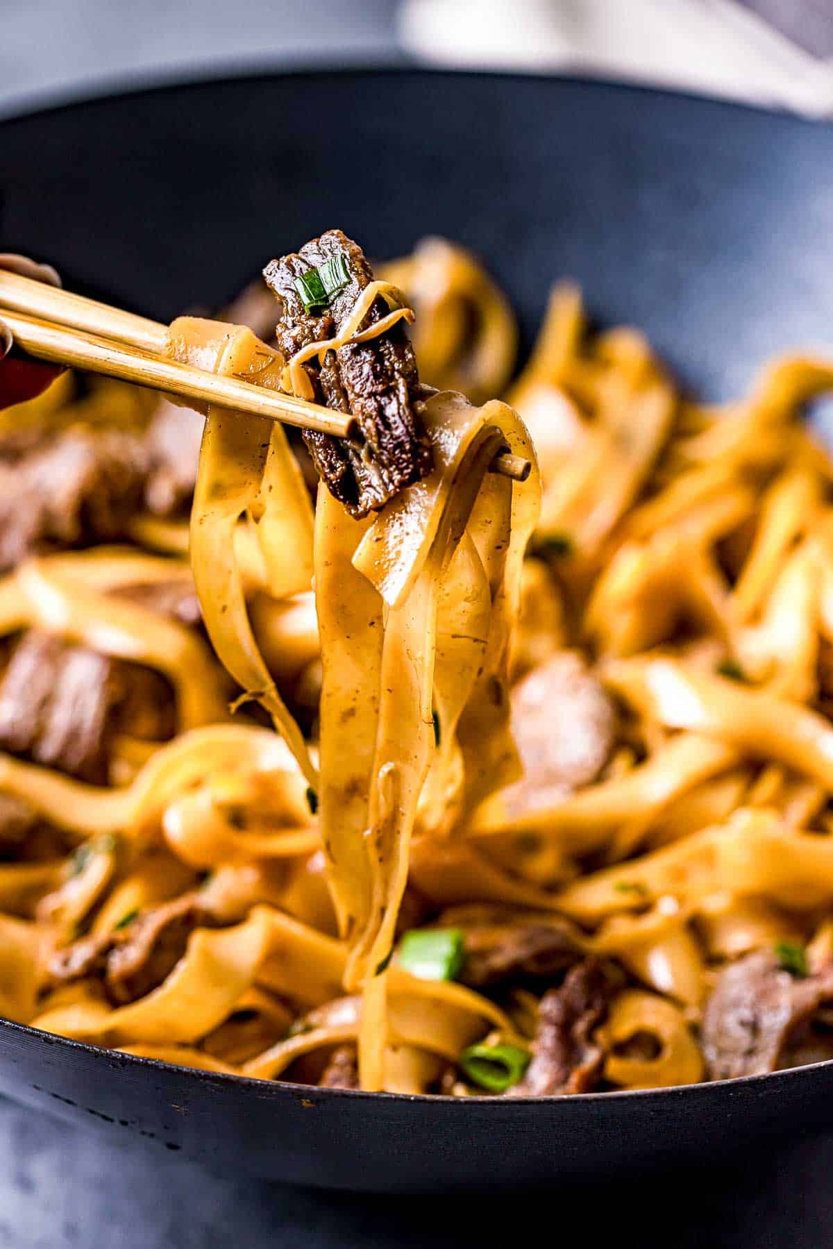 chopsticks holding beef and noodles in the air.