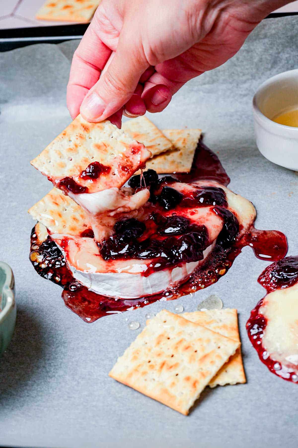 hands dipping crackers into melted brie and cranberry sauce.