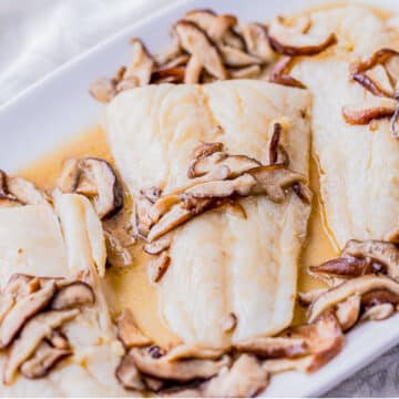 fish filets on a serving platter with mushrooms on top.