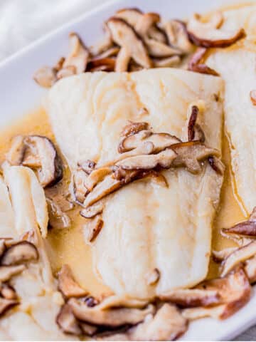 fish filets on a serving platter with mushrooms on top.