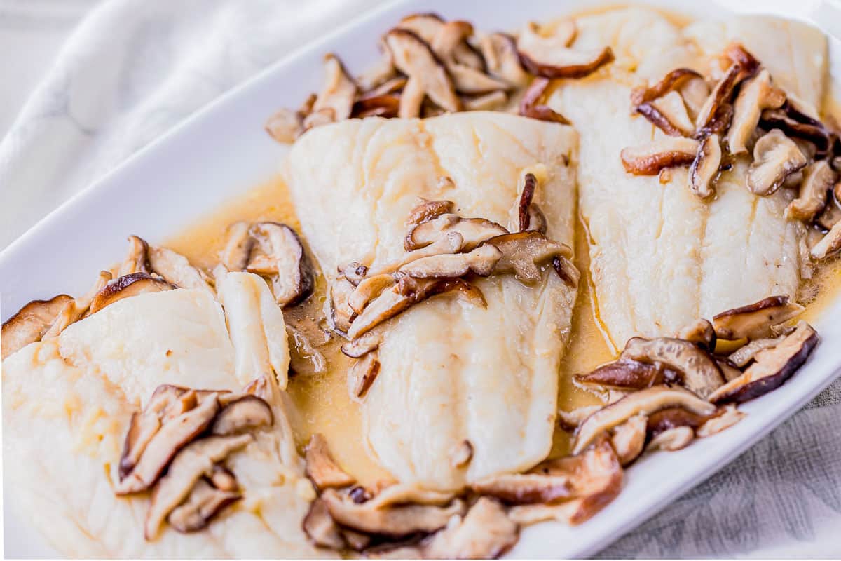 fish filets on a serving platter with mushrooms on top.