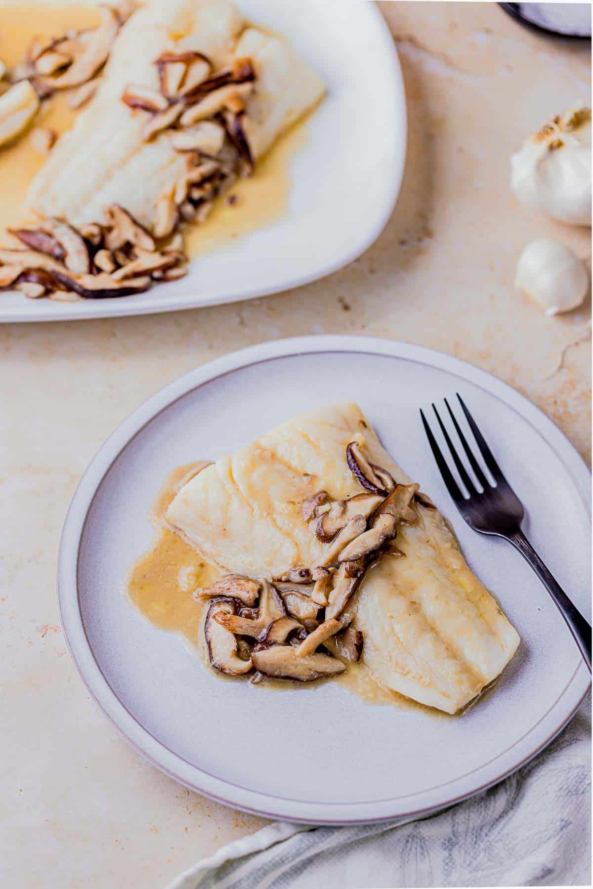 a plate with a piece of fish with mushrooms sauce.