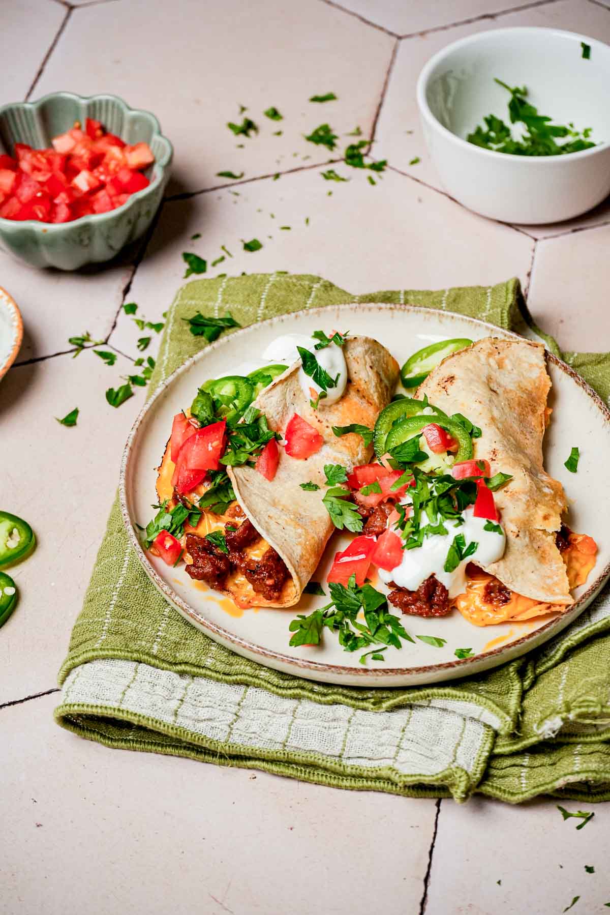 2 tacos on a plate with bowls of garnishments on the side.