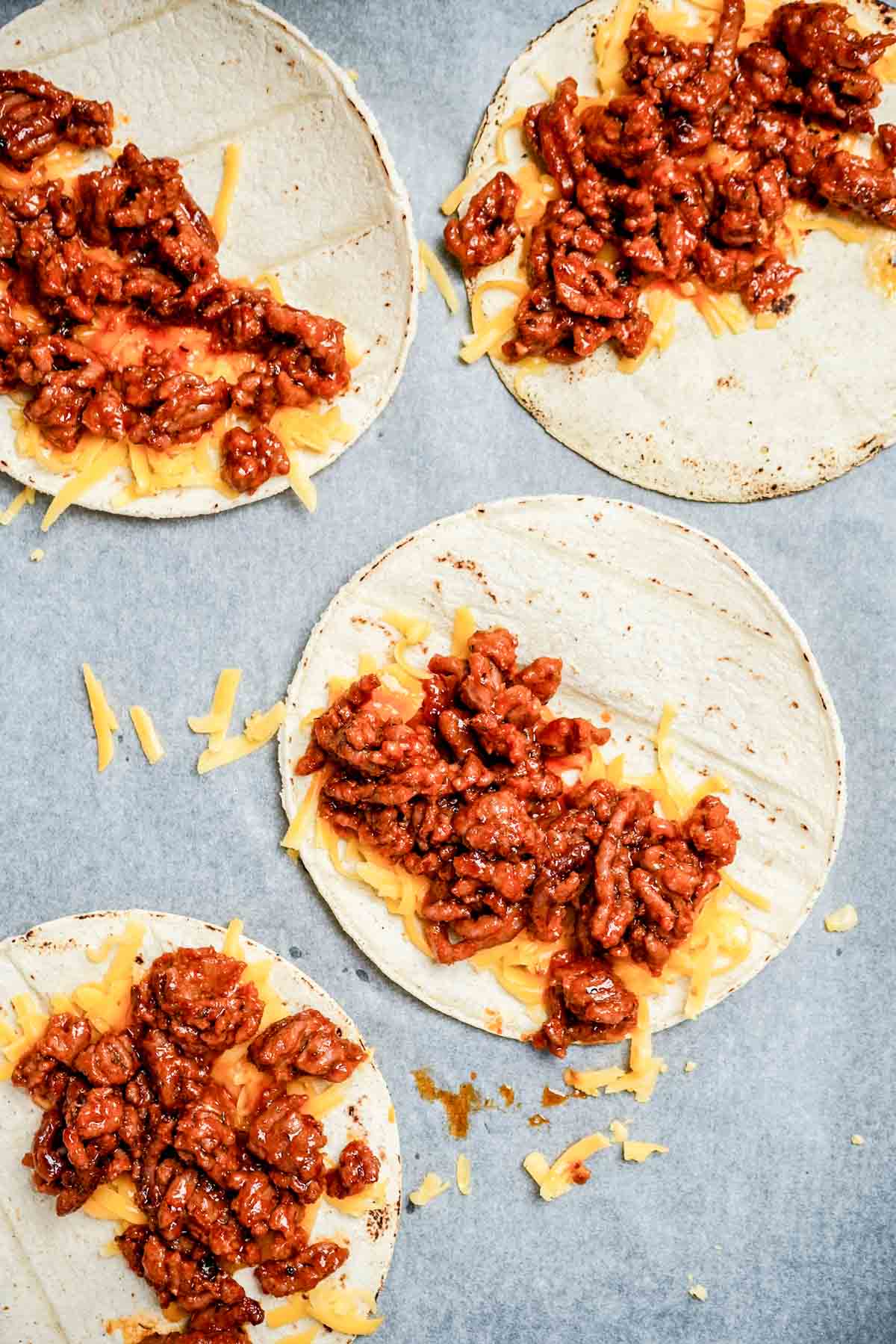 ground beef and shredded cheese on flat corn tortillas.