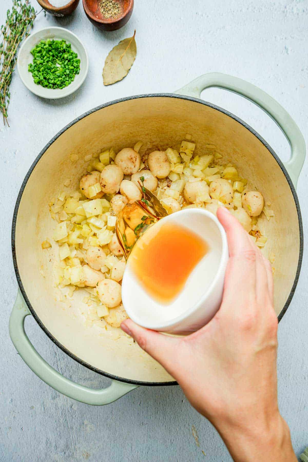 liquid being poured into a pot of cooking aromatics.