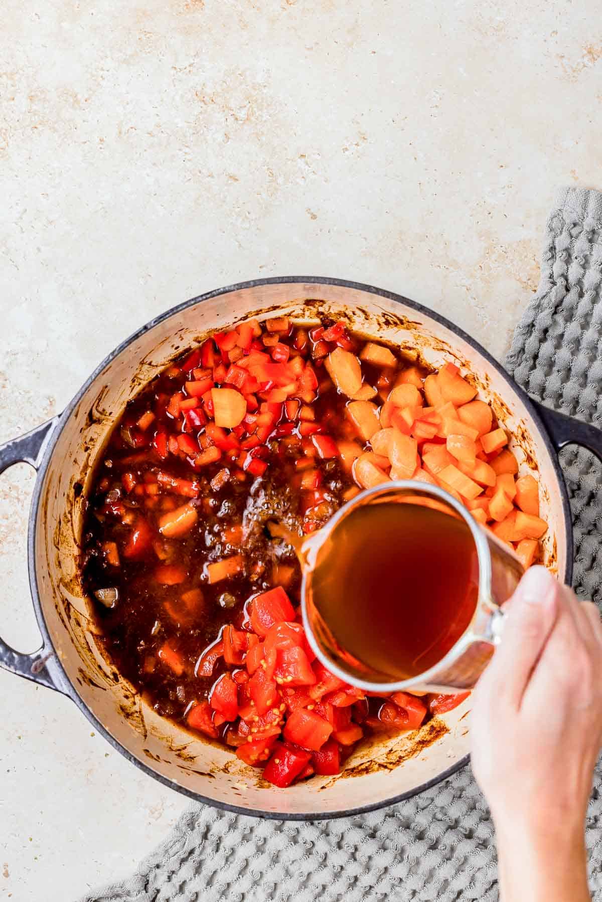 broth being poured into a pot with vegetables and beef.