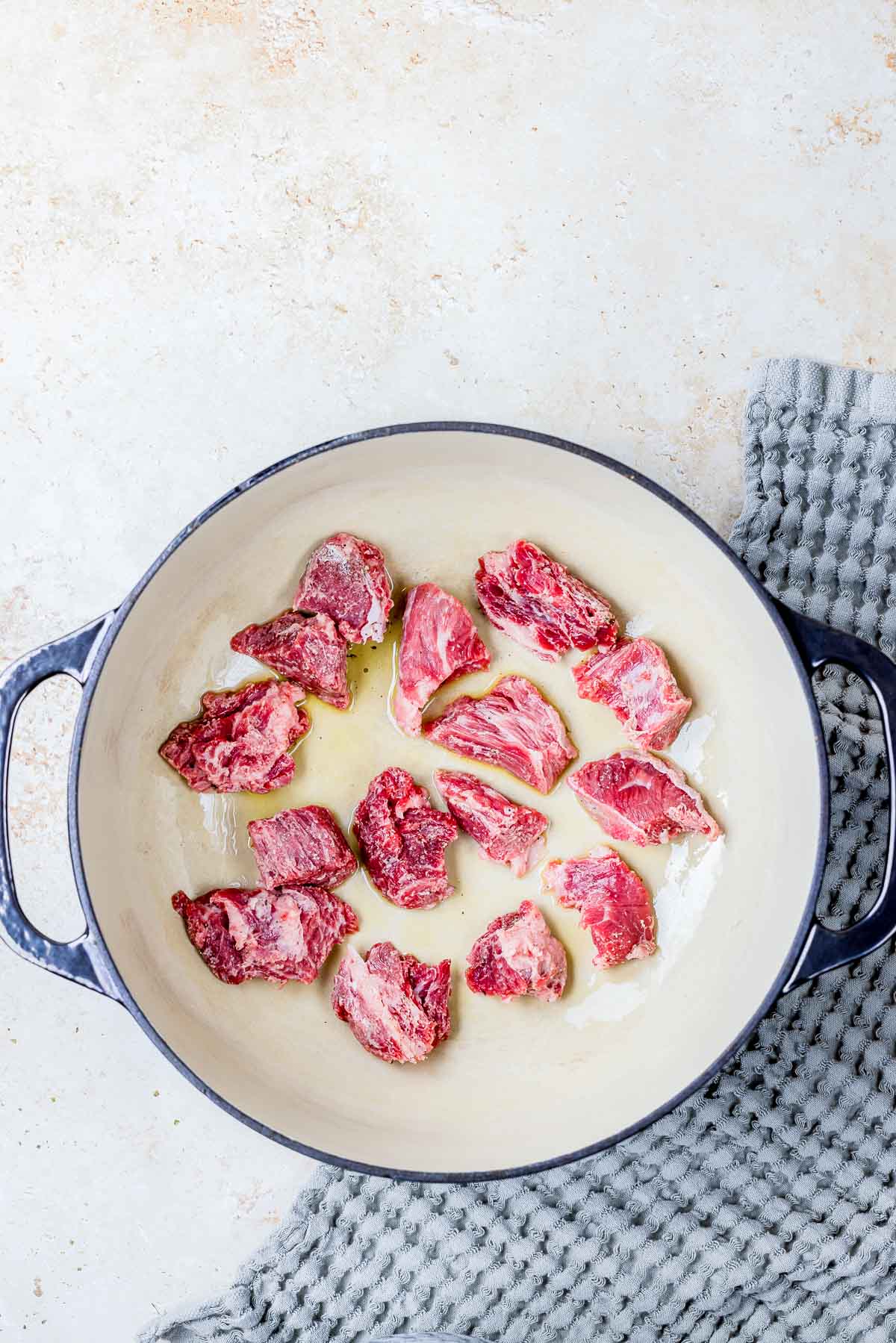 pieces of raw beef cooking in a skillet.