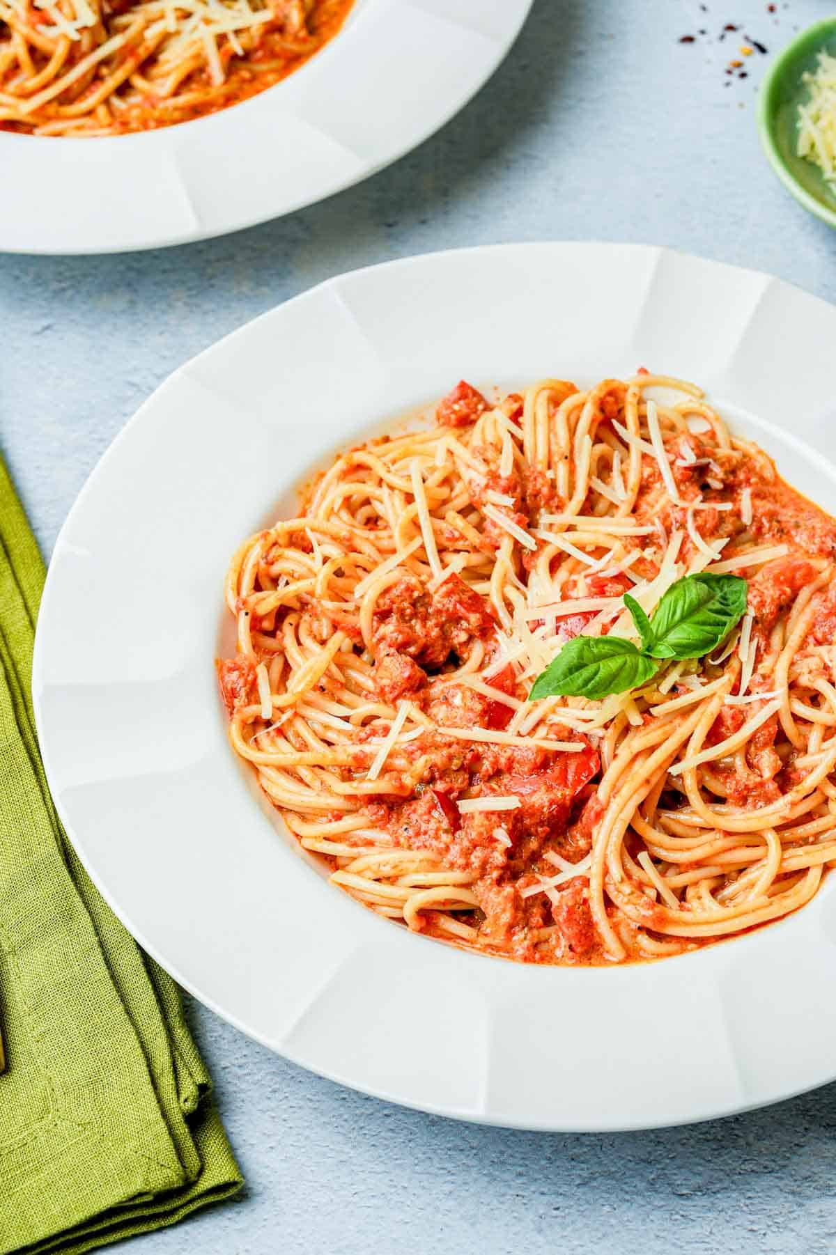 a bowl of pasta with red sauce and a basil leaf.