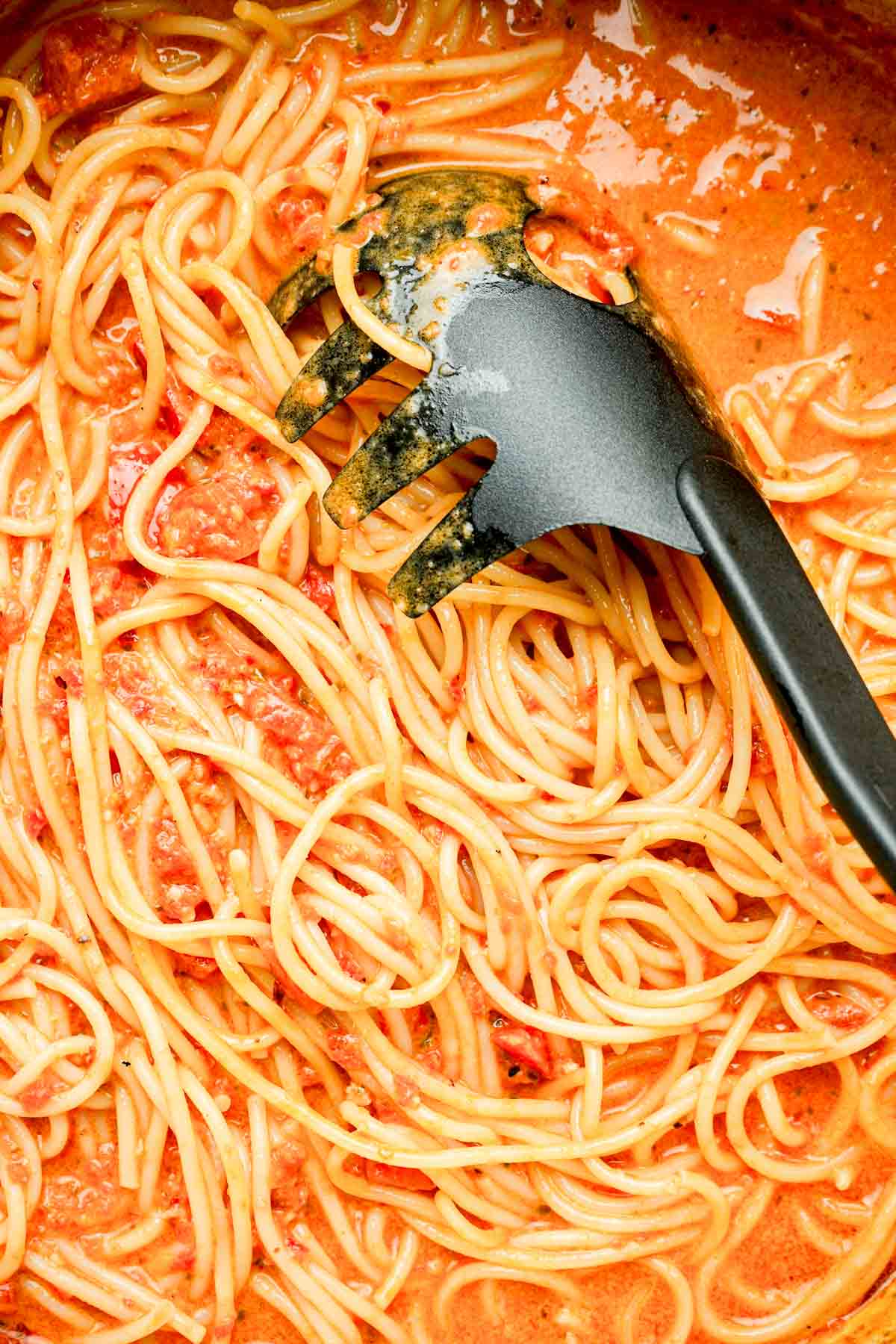 a pot of pasta in red sauce with a black serving spoon.