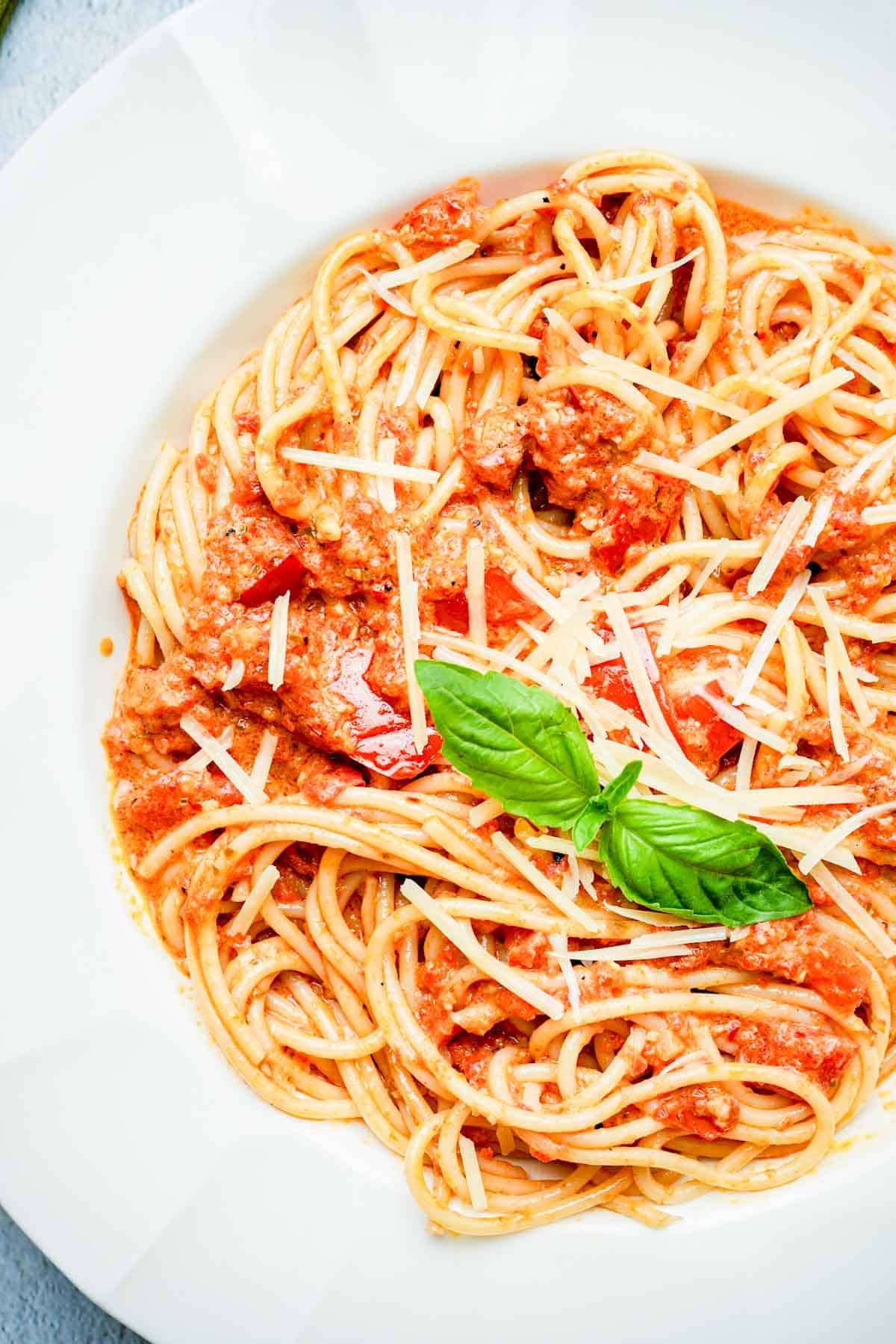 a bowl of red pepper pesto pasta with a basil leaf on top.