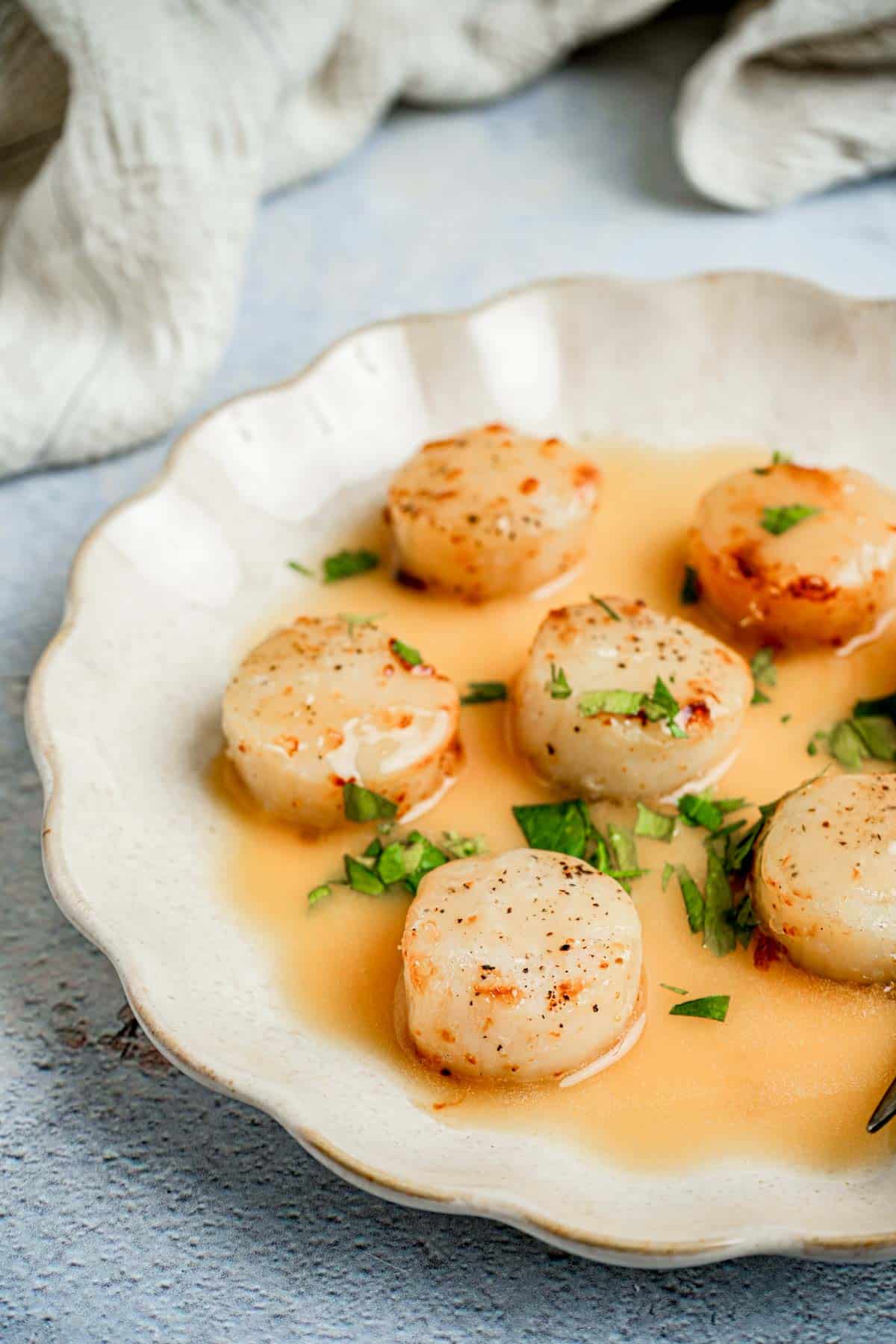 scallops in butter sauce on a plate with herbs.