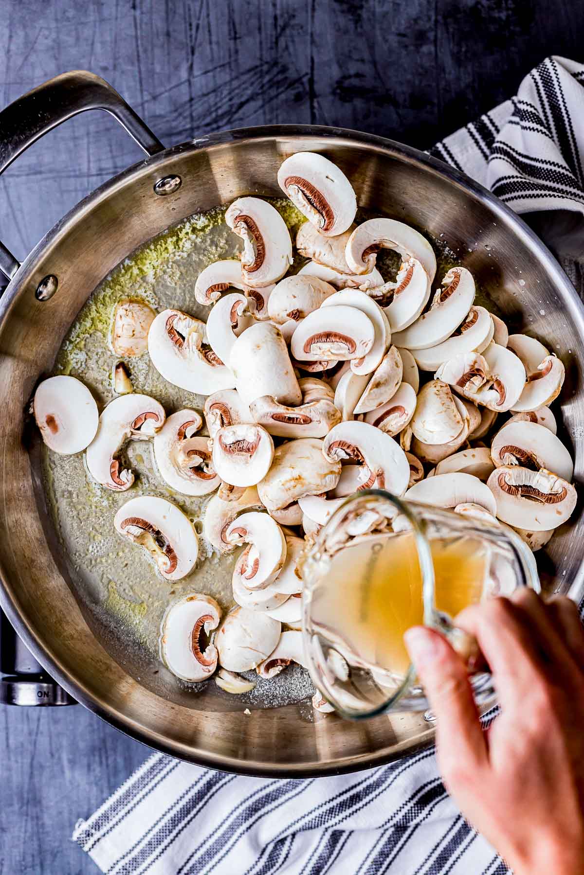 mushrooms in a skillet with liquid being poured in.