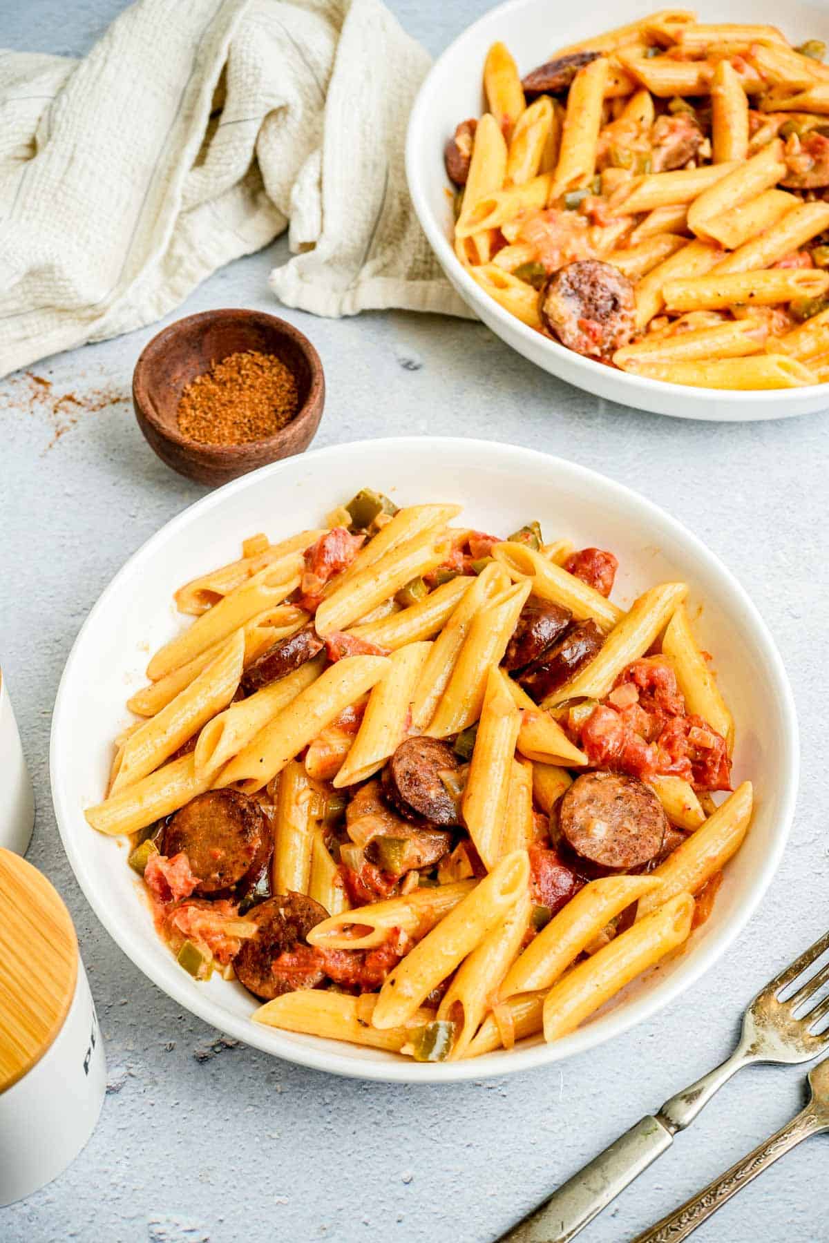 sausage and pasta in a bowl with seasoning on the side.