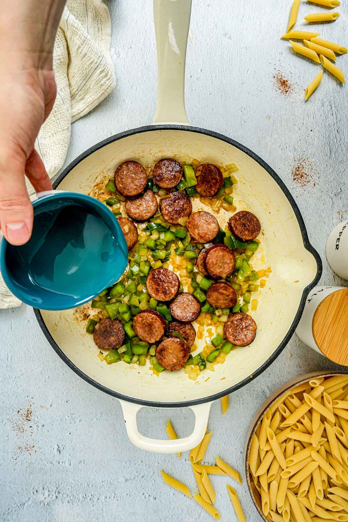 liquid being poured into a pan with sausage and vegetables.