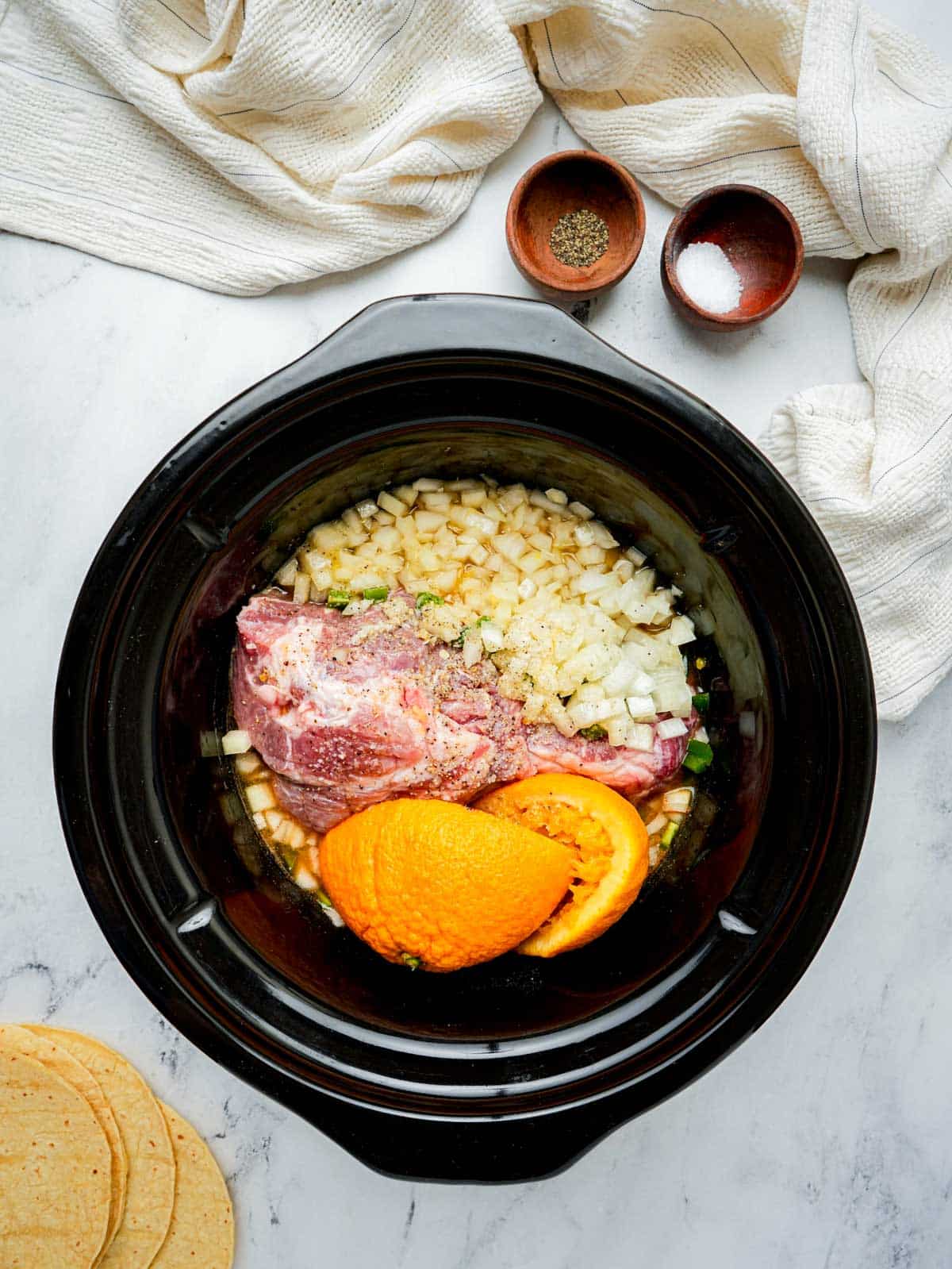 raw pork shoulder, oranges and aromatics in a slow cooker.