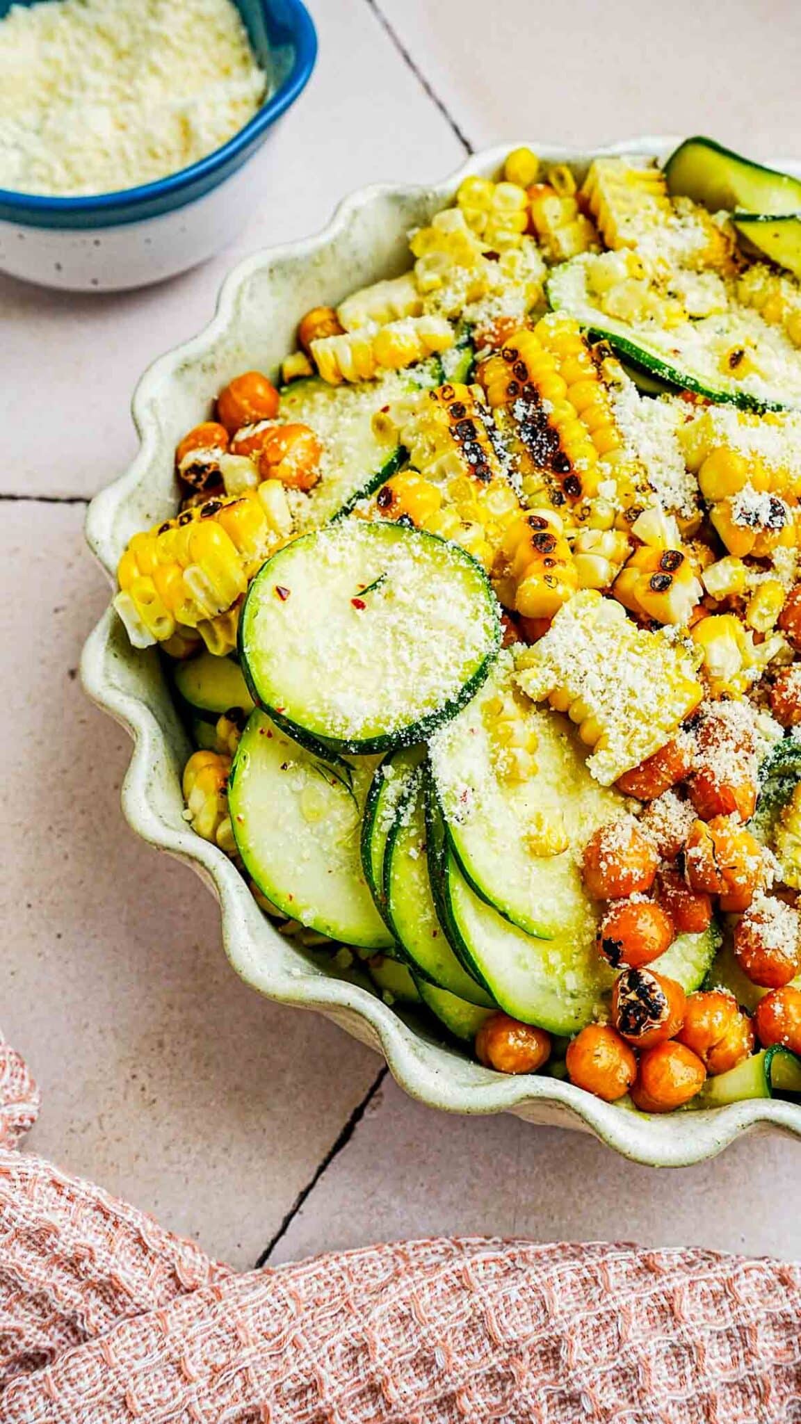 a bowl of zucchini, corn and chickpeas with cheese on top.