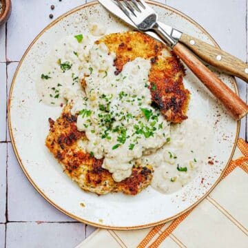 a plate of pork chops and gravy with utensils.